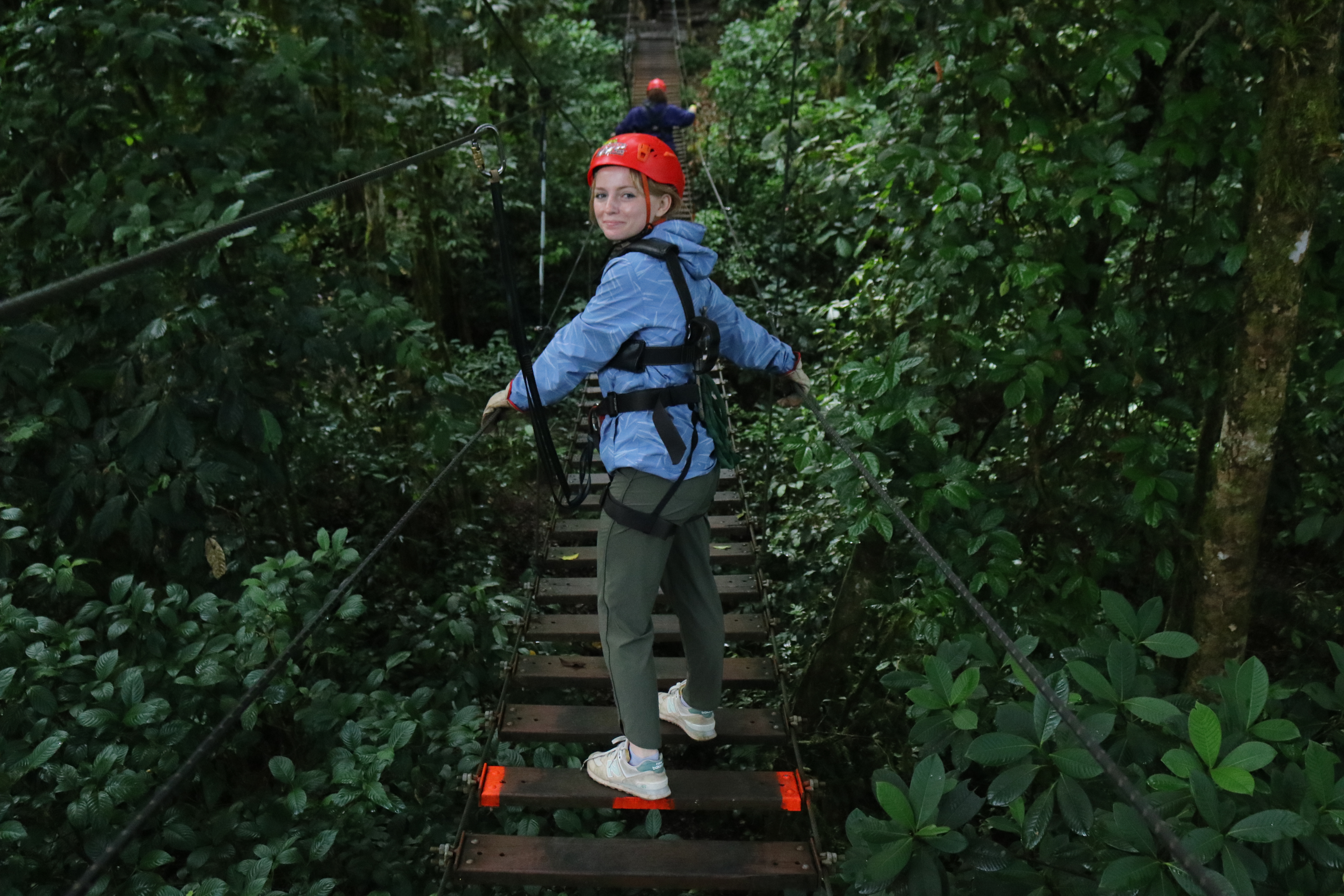 Meredith Clark in a safety helmet crossing a wooden suspension bridge in a forest