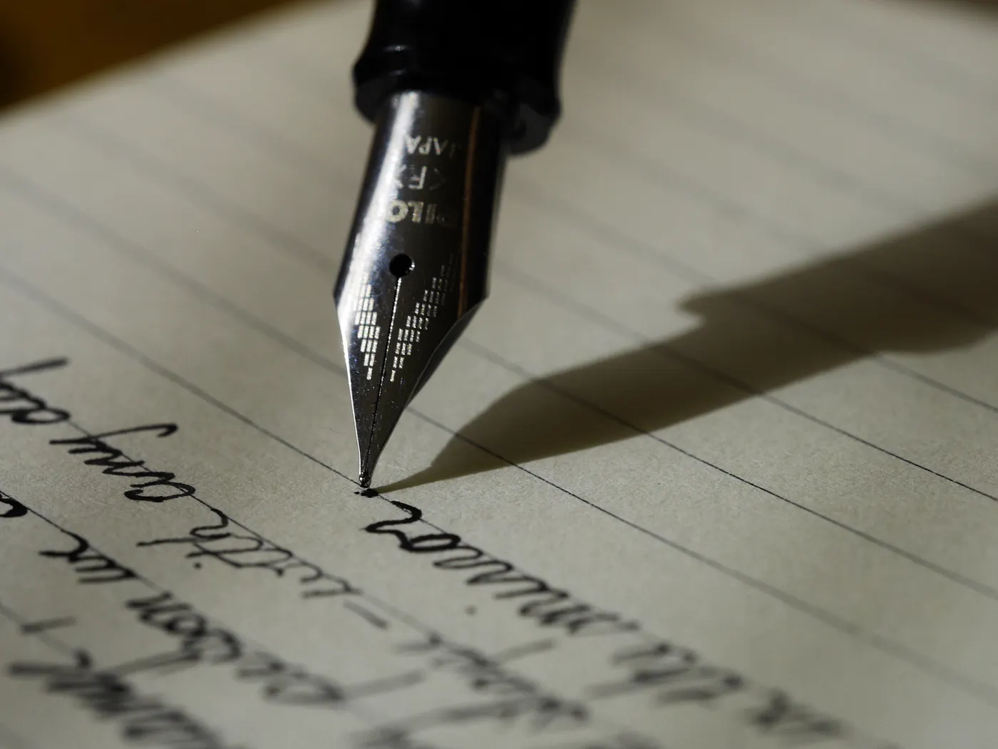 A fountain pen nib laying ink onto lined paper